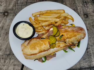 Toasted steak sandwich on a crusty baguette with pickles, fries, and creamy aioli dip