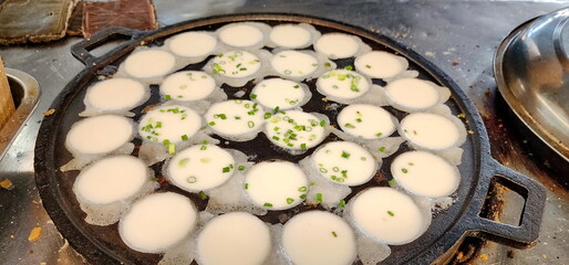 The vendor is making khanom krok in oven for making Khanom Krok. Traditional Thai desserts and sprinkling chopped green onions into the uncooked dough. Khanom Krok Pan or Thai Coconut Pudding Pan. 
 - obrazy, fototapety, plakaty