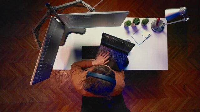 Top down view of engineer typing code in home office, using Java programming language to develop software application. It specialist using multimonitor PC setup and laptop to finish tasks, aerial shot