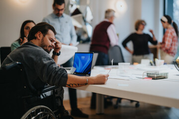 Focused team of diverse professionals, including a man in a wheelchair, collaborating in a modern office setting.