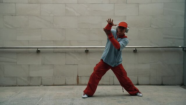 Handsome choreographer practice street dance in gray background. Young attractive b boy dancer perform while wearing stylish cloth. Feeling of lively step. Copy space. Outdoor sport 2024. Sprightly.