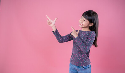 Portrait of young beautiful little asian girl hand point up isolated on pink background wall with...