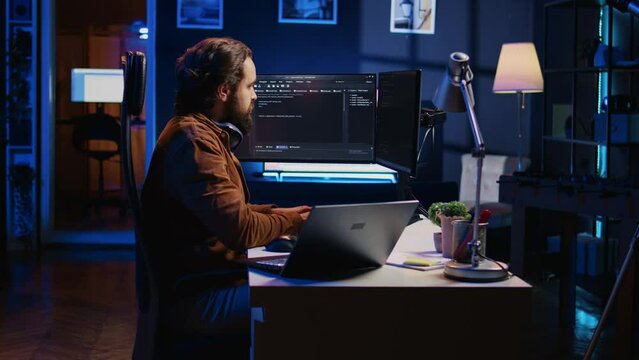 Technician typing code in neon lit personal office, using javascript programming language to develop software application. It specialist using multimonitor desktop setup to finish project, camera B