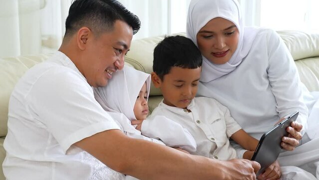 Happy muslim family watching video streaming together on a digital tablet while sitting on sofa