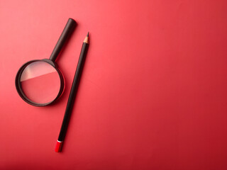 Top view pencil and magnifying glass on a red background