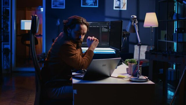 Software programmer putting headphones on while developing code, making time pass faster during remote job shift. IT professional doing multitasking in apartment office while listening music, camera B