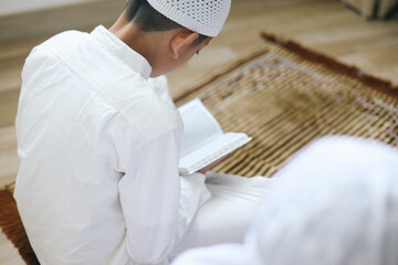 Rear view of moslem boy reading Quran while sitting on prayer mat