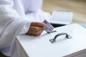 Hand of muslim girl putting the money into donation box