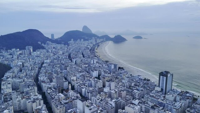 Aerial shot drone flies to the left high over Copacabana at dawn with clouds blocking the sunrise