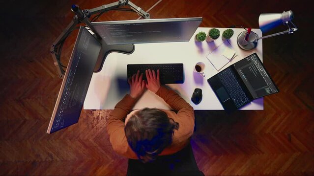 Top down view of technician puts headphones on while fortifying firewalls, teleworking for IT company. Computer scientist listening music and upgrading binary code scripts in home office, aerial shot