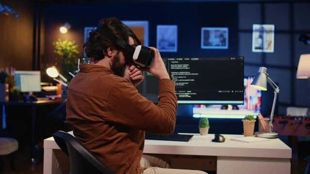 Remote software developer using VR goggles in personal office at home to do javascript programming. IT engineer wearing virtual reality headset in order to visualize lines of code, camera B