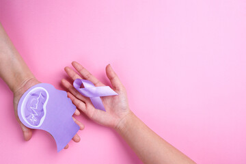 Hands holding purple ribbon with human brain paper cutout on pink background.