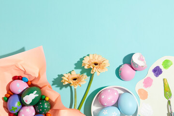 View from above of a vibrant collection of colorful painted striped Easter eggs decorated with candies, flower branches and a palette knife. Blue background. Copy space for banner or poster design