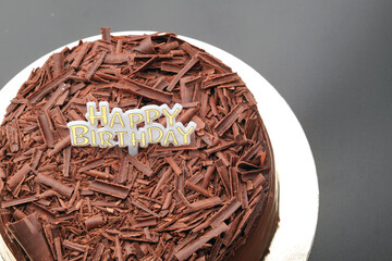 A dark black forest chocolate cake with a Happy Birthday sign sits on a black background
