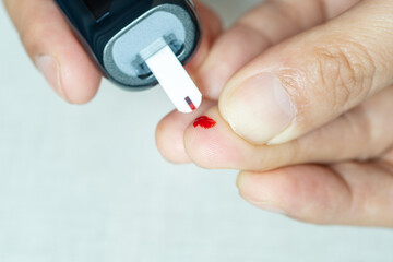 A man draws blood and checks for diabetes and high blood sugar levels with a digital blood sugar tester. Health care and medical concept