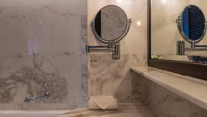 Details of the bathroom interior. Beige tiled walls, two mirrors- rectangular and round magnifying....