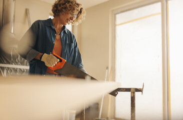 DIY home improvement with a saw: Woman performing trim work and molding installation during kitchen...