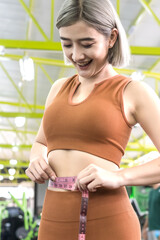 sportswoman measuring her waist with measuring tape in gym