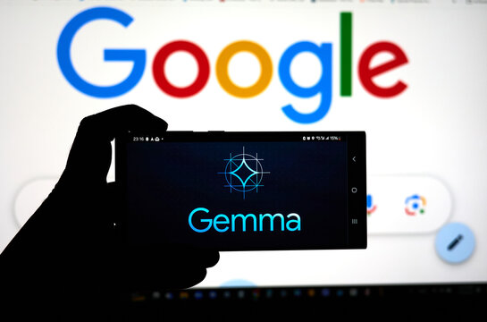 A hand holding a cellphone with Google Gemma logo over Google screen