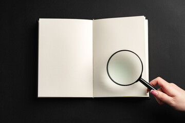 Notebook and magnifying glass on black background