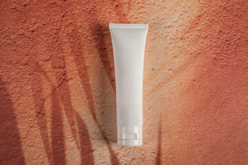 Cosmetic cream tube in womans hand on placement background with palm shadow. Beauty concept
