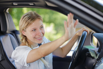beautiful young cheerful woman waving while sitting in her car