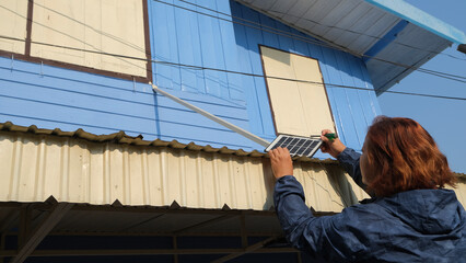 A woman installs solar panels on a garage roof by herself.
