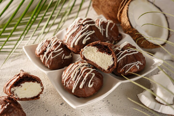 Chocolate profiteroles, eclairs, with coconut cream on a light background, on the background of green palm leaves