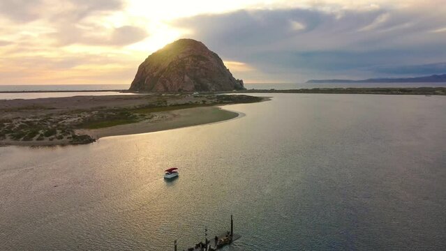 Sunset in Morro Bay, aerial view of morro rock, boat in the inlet sea, sea lions on a wooden jetty. Orange light, cloudy. Ascending motion