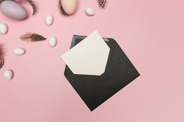 Top view of easter eggs, feathers, black envelope and white card on pink background. Creative easter composition, spring, flat lay, copy space.