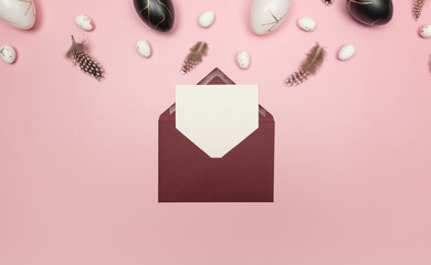 Top view of easter eggs, feathers, red envelope and white card on pink background. Creative easter composition, spring, flat lay, copy space.