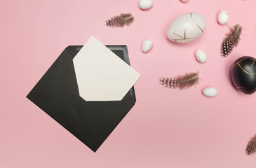 Top view of easter eggs, feathers, black envelope and white card on pink background. Creative...