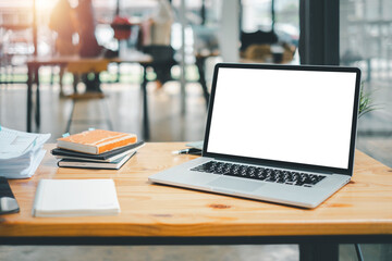 An organized work setup featuring a laptop with a blank screen, notebooks, and a plant on a wooden table in a bright office.