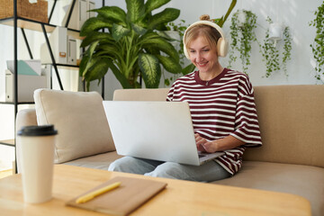 Excited woman wearing headphones when working on laptop from home