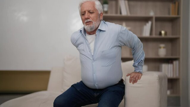 Senior man tries to stand from armchair. Elderly male suffering atherosclerosis, arthritis, osteoporosis disease. Health problems in old age, stiffness of movements, painful sensations in lower back.