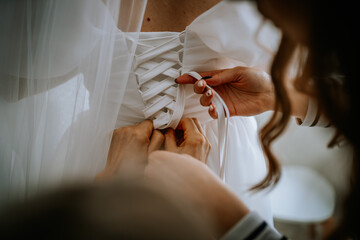 Riga, Latvia - January 20, 2024 - hands tying the ribbon on the back of a white bridal gown, with a...