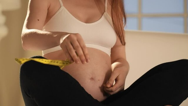 Pregnant woman measuring her belly. Unrecognizable pregnant woman measuring belly diameter with yellow measure band tape, monitoring body changes weight gain dimensions. Pregnancy maternity concept.