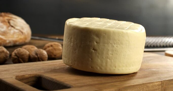 Super slow motion macro of traditional italian bio organic toma cheese is falling on rustic wooden chopping board in kitchen of restaurant  or dairy farm at 1000 fps.