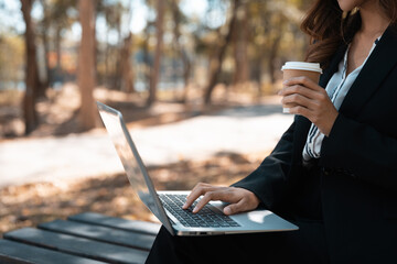 Young woman in formal suit drinking coffee and using laptop during working remotely in park