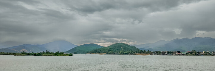 Wide panoramic view of a serene lake with distant mountains under an overcast sky, perfect for tranquil nature-themed backgrounds with ample space for text