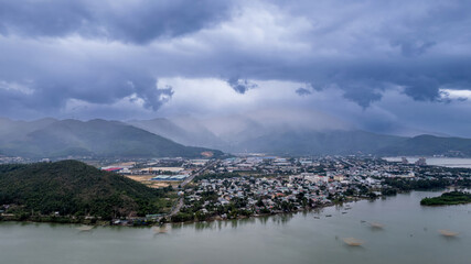 Aerial view of a tranquil river winding through a developing Asian cityscape with misty mountains...