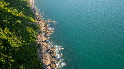 Aerial view of a lush coastline with rocky shores meeting the clear turquoise sea, perfect for travel and nature-themed backgrounds