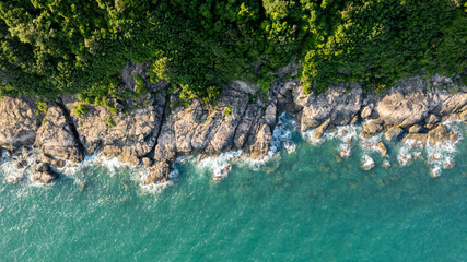 Aerial view of a rocky coastline with lush green forest meeting turquoise sea waters, ideal for travel and nature-themed backgrounds, Earth day concept