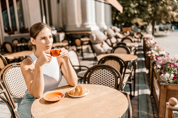 Portrait of happy woman sitting in a cafe outdoor drinking coffee. Woman while relaxing in cafe at table on street, dressed in a white T-shirt and jeans