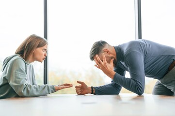 Couple are having quarrel. Woman is sitting by the table, man is standing