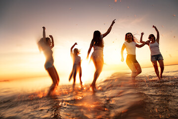 Group of happy young girls are having fun and dancing at calm sunset beach. Blurred motion