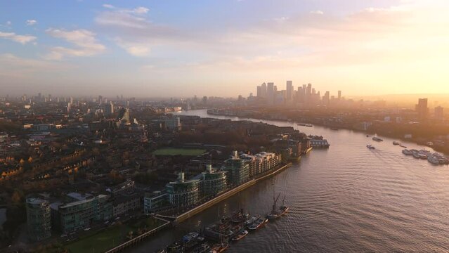 As the sun sets, aerial London skyline and Thames River are shining against the vibrant sky, showcasing a tranquil transition from day to night in the city. The calm river mirrors the fading light
