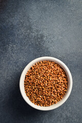 Close-up of buckwheat groats in a bowl. On a dark concrete background. - obrazy, fototapety, plakaty