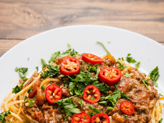 Spaghetti Bolognese dish with pasta, red sauce, minced beef, red peppers and green fresh herbs on white plate and light color table cloth. High quality products in a tasty Italian style dish.