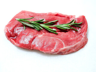 One uncooked boneless lamb leg steak with green fresh rosemary herb on white background. Premium high quality meat product of agriculture industry. Butcher craft and skill. Food supply chain.